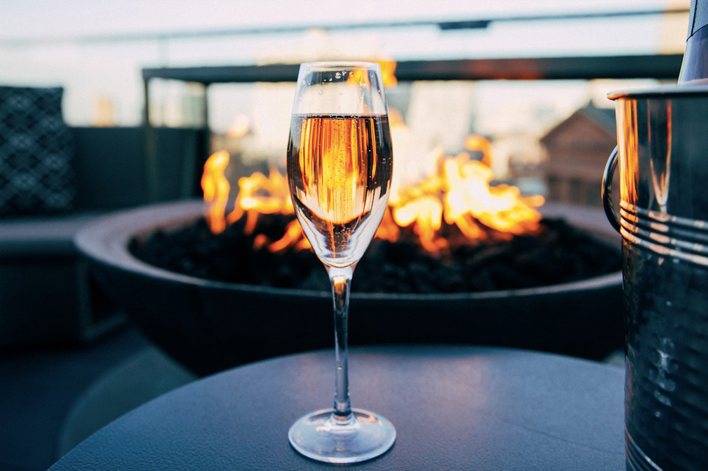 a glass of champagne at Bok Bar, with a fire in the background on the rooftop