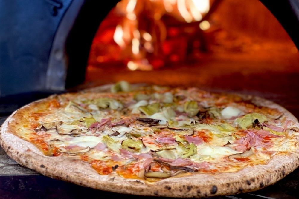 A pizza coming out of a wood-fired oven