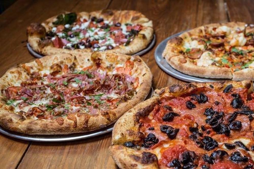 Four different pizza pies on a wood surface