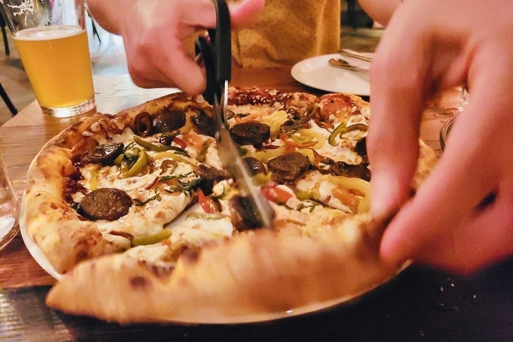 A loaded pizza being cut into slices with scissors