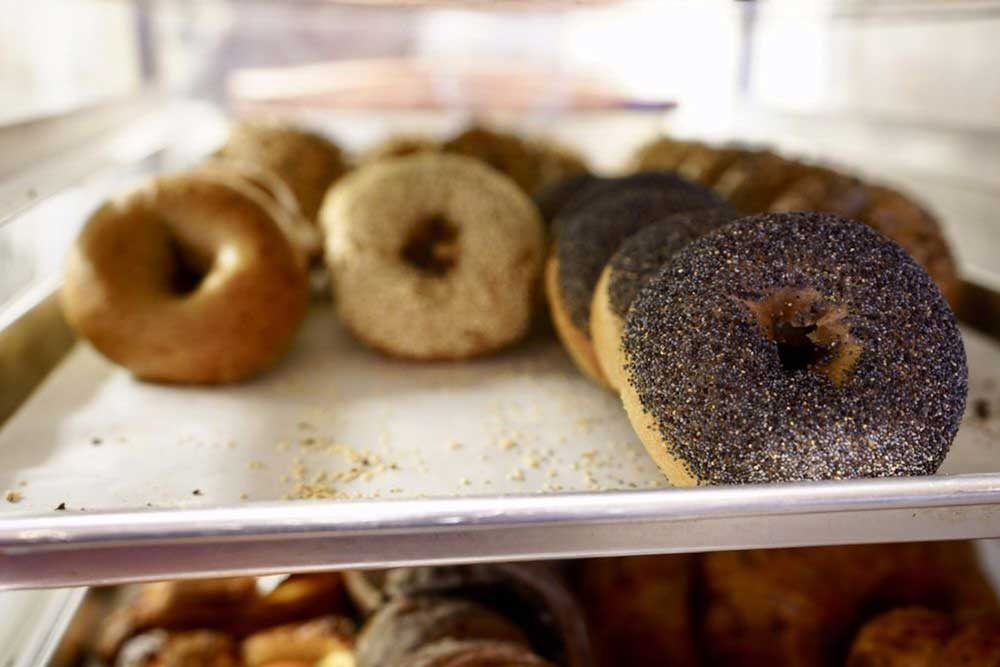 Several bagels on a sheet tray, with poppy seed bagels closest to the camera