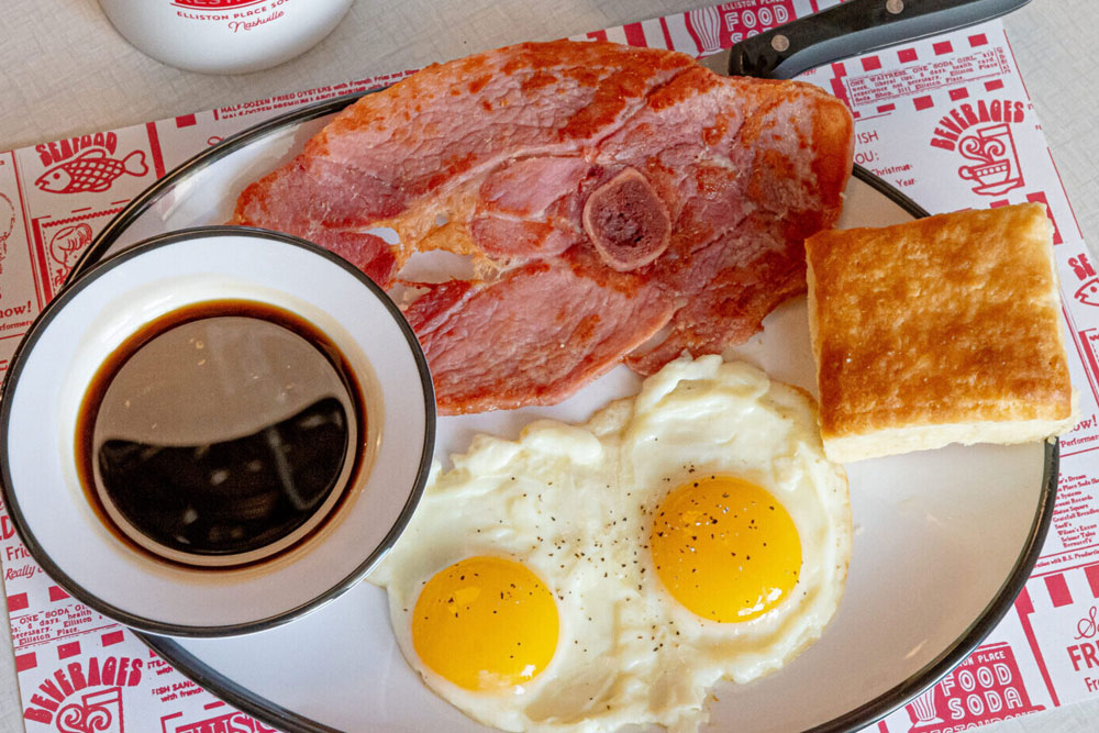 a breakfast plate with classic eggs, ham, a biscuit, and syrup from Elliston Place Soda Shop in Nashville