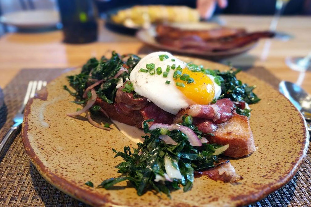 Toast with an egg and greens on top on a sand-colored plate