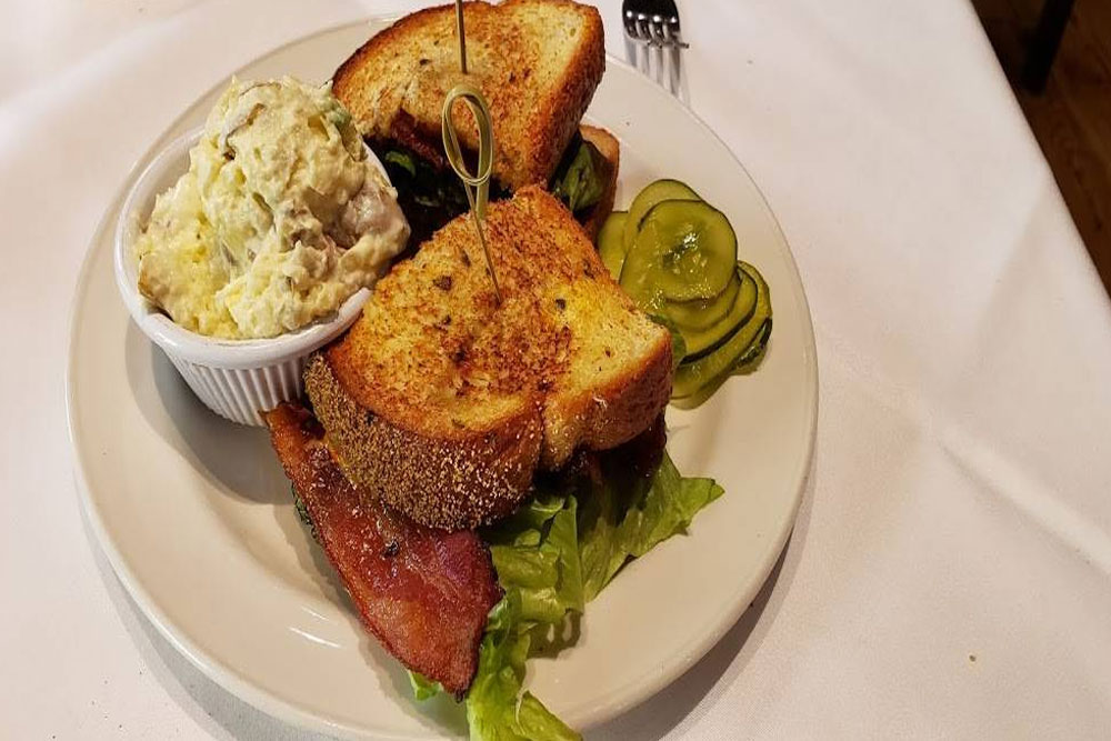 An overhead shot of a sandwich cut in half with potato salad and pickles on the side