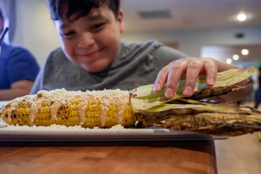 Elote at Cocina Madrigal. A boy smiles in the background, touching the corn husks.