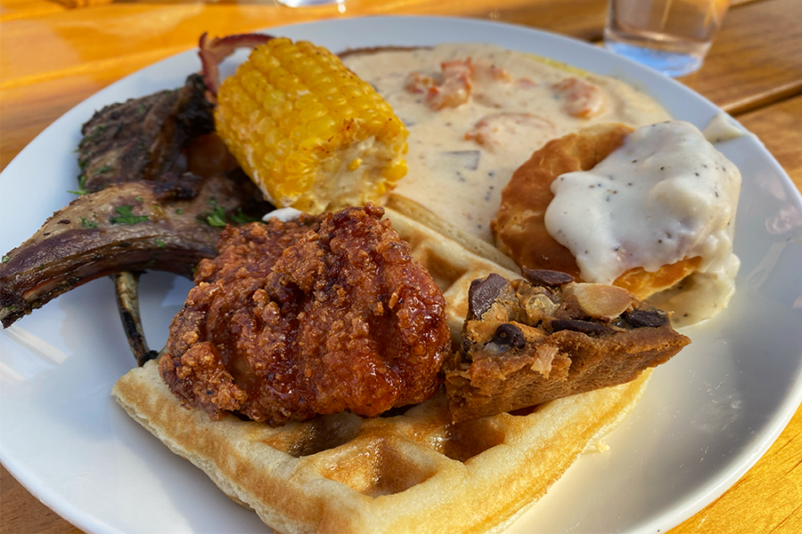 Plate full of breakfast foods, including lamb chops, waffles, biscuits, fried chicken, corn, and more
