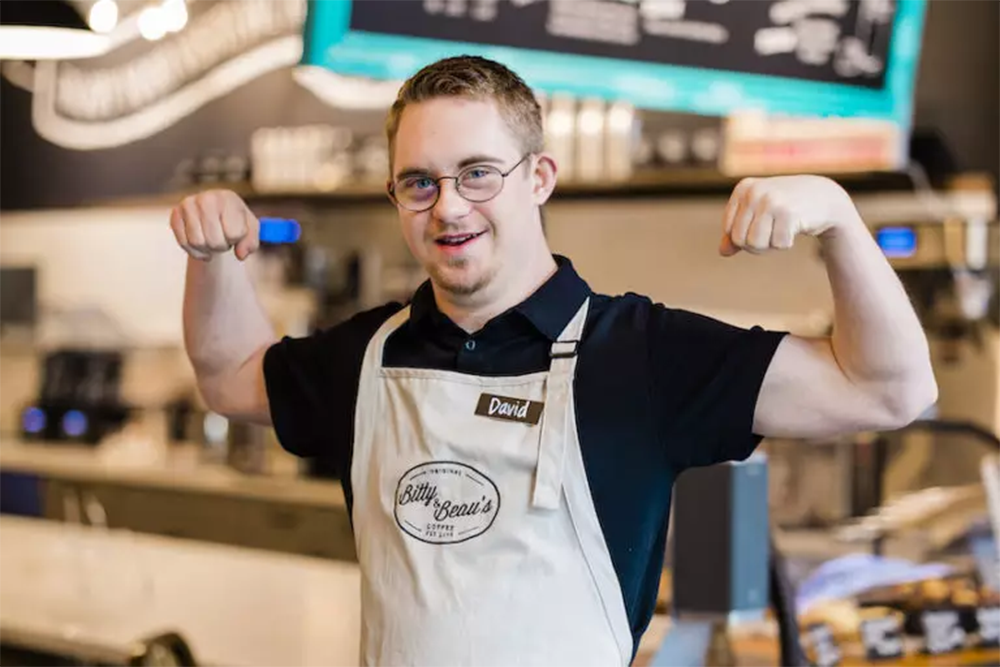 A man flexing his arms while wearing an apron and name tag that says David