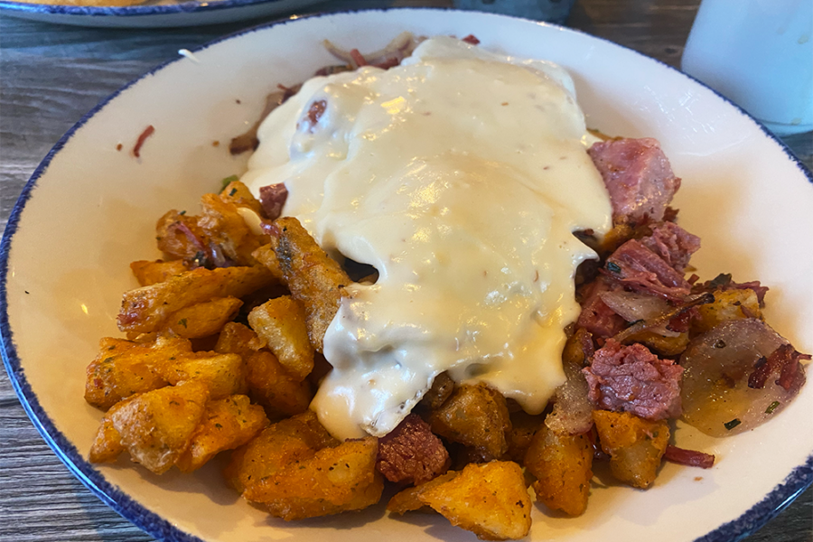 Hash with crispy potatoes, corned beef, onions, eggs, and a gouda sauce on top