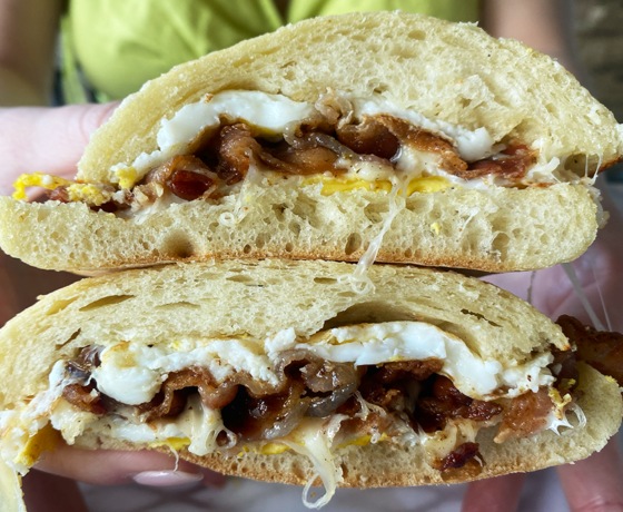 A breakfast sandwich sliced in half and facing the camera, each half topped with fried egg, white cheese, and bacon