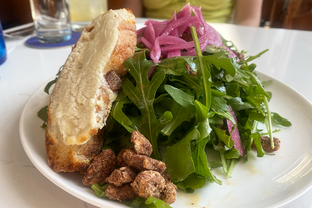 Arugula salad with pickled onions, candied nuts, and a slice of bread with cheese crusted on top