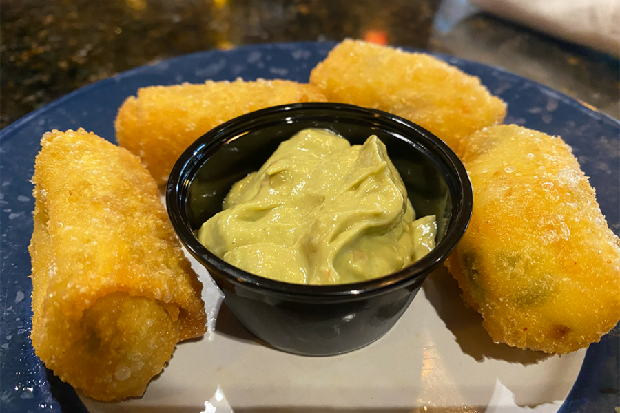 Four golden wontons gathered around a black cup of green sauce