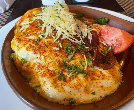Brown pan with a gravy-covered open-faced sandwich topped with bacon and parmesan cheese