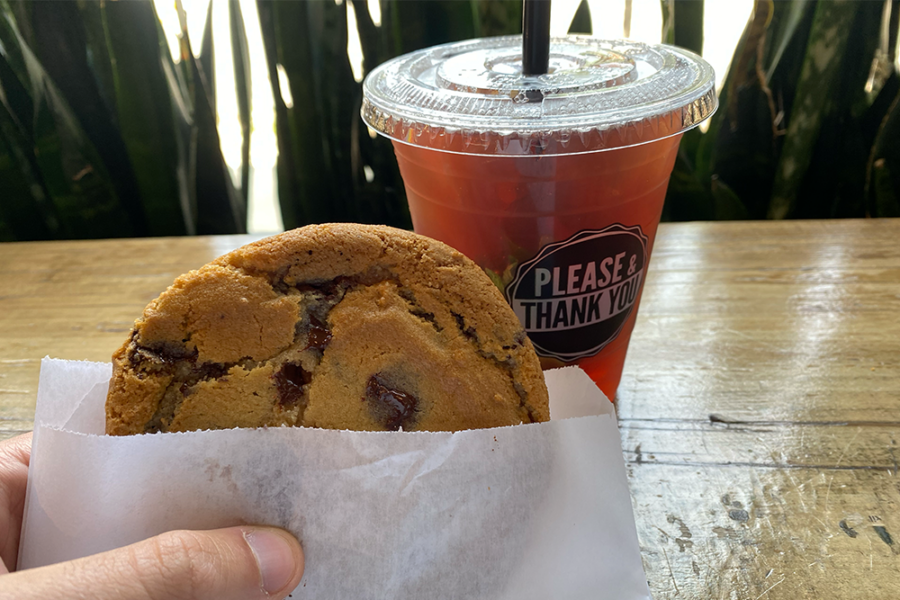 Chocolate chip cookie in a paper sleeve held up in front of an iced tea with a label saying "Please & Thank You"