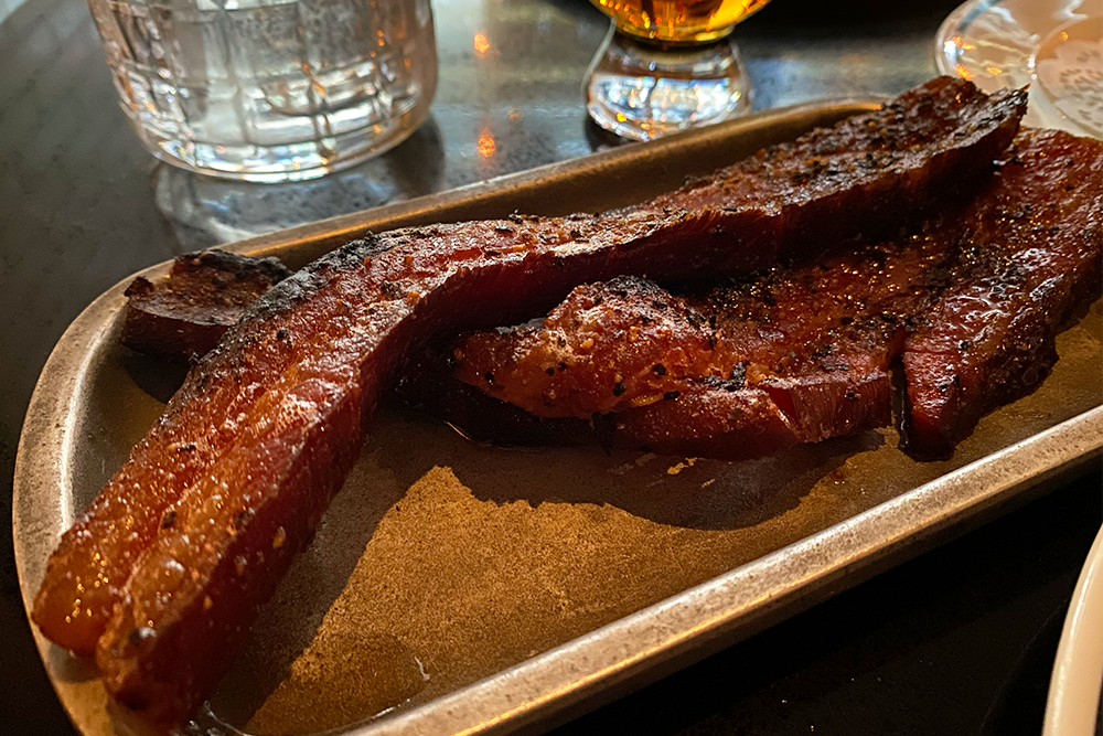 Two long skinny slivers of peppered bacon on a silver tray