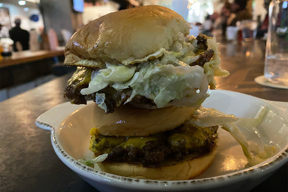 A slider stacked on top of another, both with lettuce, cheese, and more on a plate