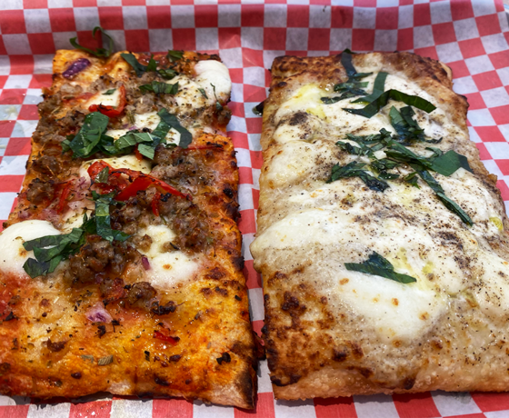 Two slices of rectangular pizza, one with red sauce and the other with white, both topped with basil