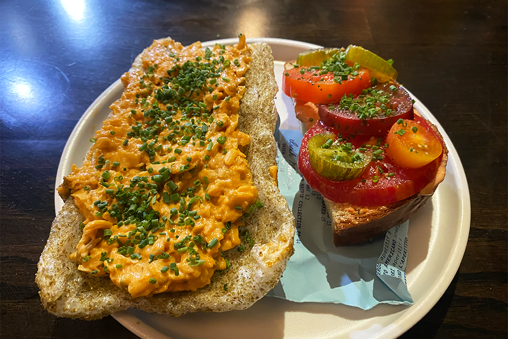 Piece of fried pork with pimento cheese on top next to a slice of bread with red mayo and sliced tomatoes