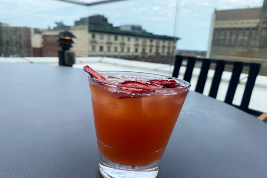 Brown-red drink with dehydrated strawberries on top on a table with a view of buildings in the background